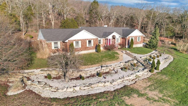 ranch-style house with driveway, a front lawn, a wooded view, and brick siding