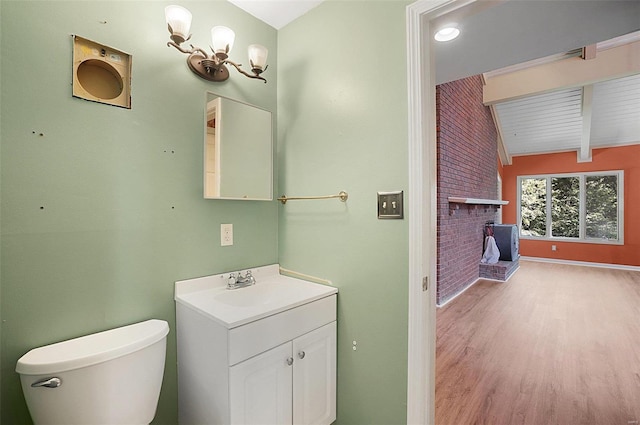 bathroom with hardwood / wood-style floors, vanity, a brick fireplace, vaulted ceiling with beams, and toilet