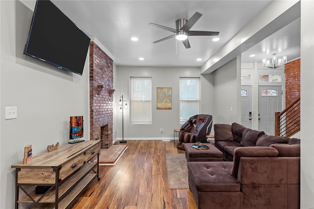 living room with hardwood / wood-style floors, ceiling fan with notable chandelier, and a brick fireplace