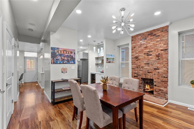 dining area with wine cooler, a fireplace, wood-type flooring, and a notable chandelier