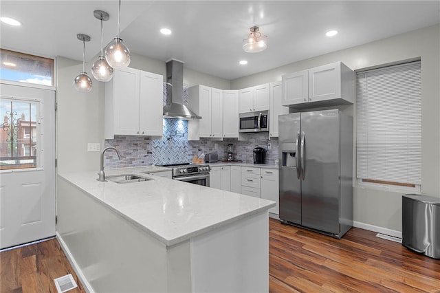 kitchen featuring kitchen peninsula, wall chimney exhaust hood, stainless steel appliances, sink, and white cabinets