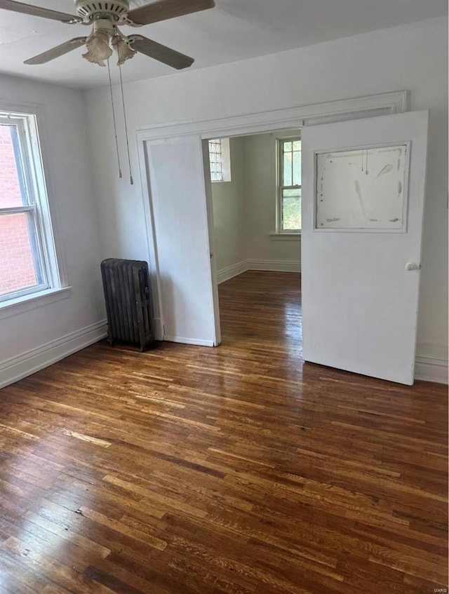 unfurnished room with plenty of natural light, radiator, dark wood-type flooring, and ceiling fan