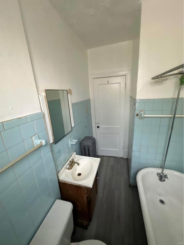 bathroom featuring radiator, a bath, wood-type flooring, vanity, and tile walls