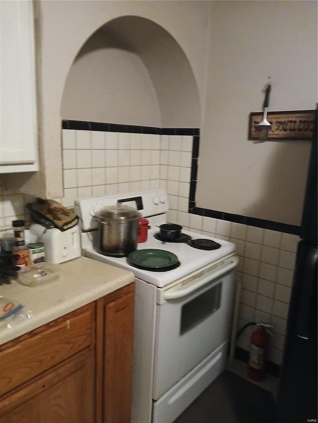 kitchen featuring brown cabinets, tile walls, white electric range oven, light countertops, and freestanding refrigerator