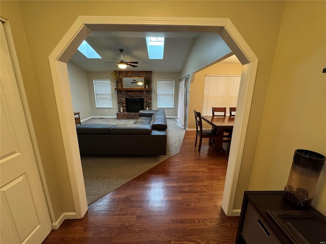 bedroom featuring ceiling fan, vaulted ceiling with skylight, dark hardwood / wood-style floors, and a brick fireplace