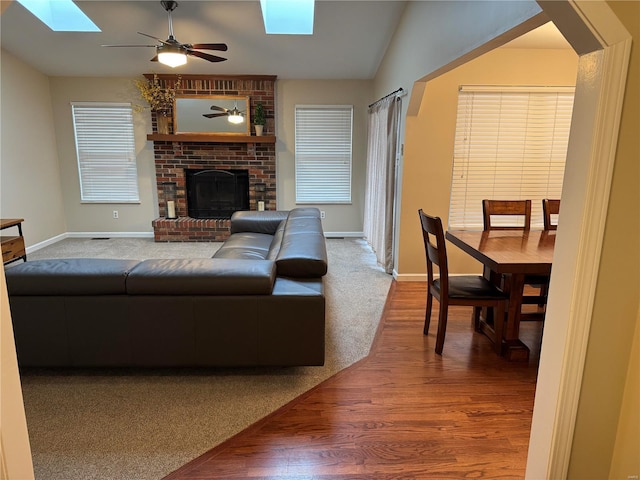 living room featuring a fireplace, wood-type flooring, ceiling fan, and vaulted ceiling with skylight