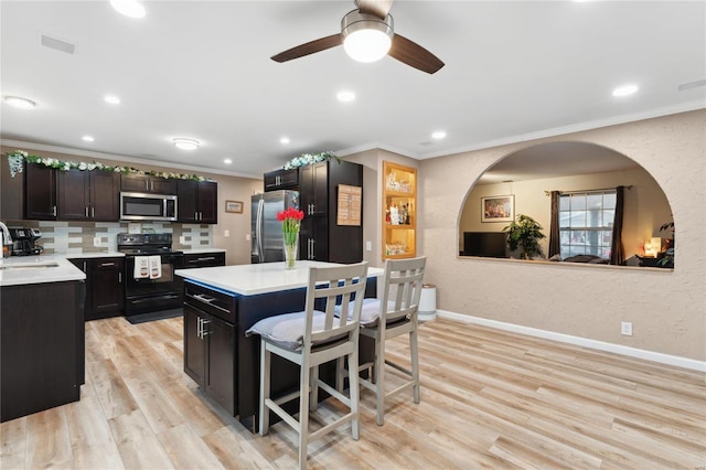 kitchen featuring a kitchen breakfast bar, ornamental molding, stainless steel appliances, light hardwood / wood-style floors, and a kitchen island