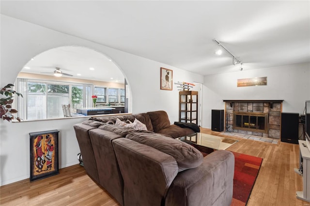 living room with light wood-type flooring, rail lighting, a stone fireplace, and ceiling fan