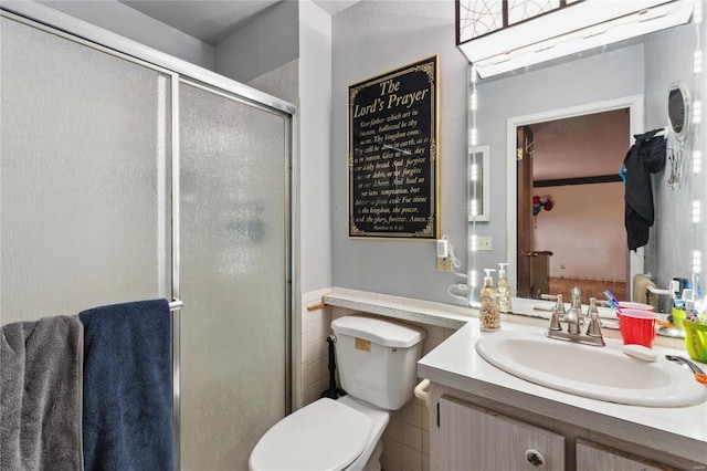 bathroom with vanity, a shower with shower door, tile walls, and toilet