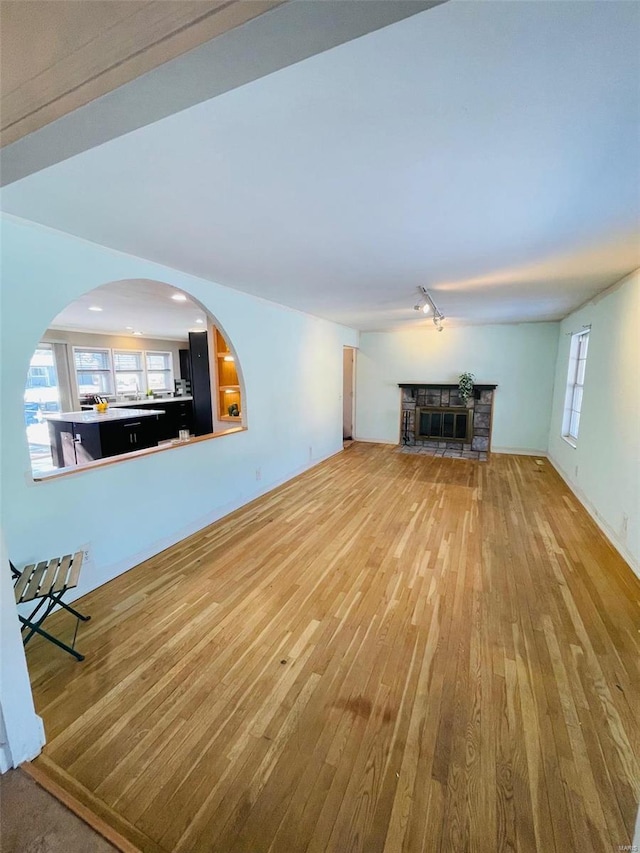 unfurnished living room with rail lighting, a stone fireplace, plenty of natural light, and hardwood / wood-style floors