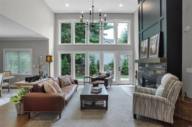 living room with a high ceiling, an inviting chandelier, a stone fireplace, and a healthy amount of sunlight