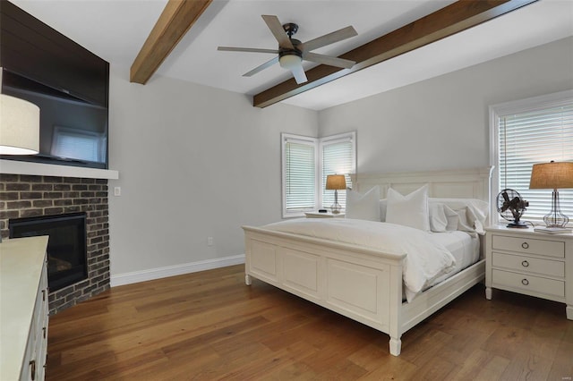 bedroom with beam ceiling, ceiling fan, dark wood-type flooring, and a brick fireplace