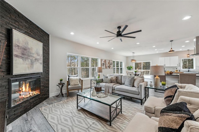 living room with ceiling fan, a large fireplace, light wood-type flooring, and sink