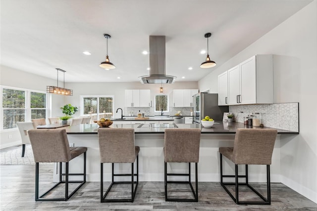 kitchen with white cabinets, stainless steel fridge, island range hood, and a breakfast bar