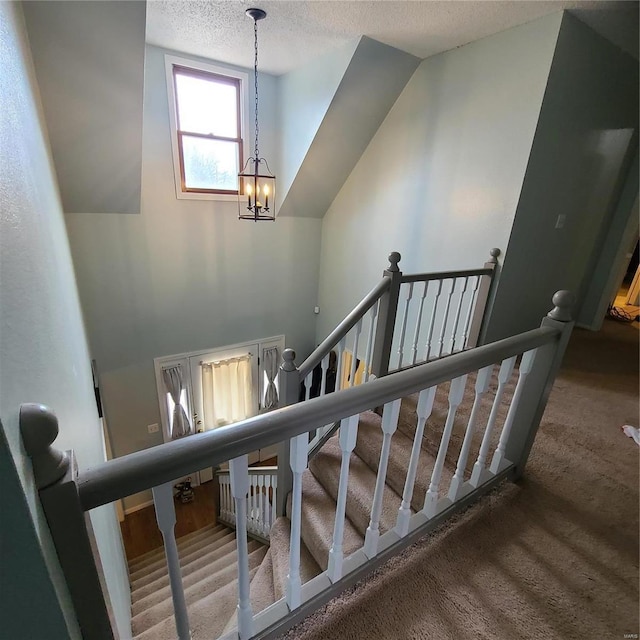 staircase featuring a chandelier, a textured ceiling, and vaulted ceiling