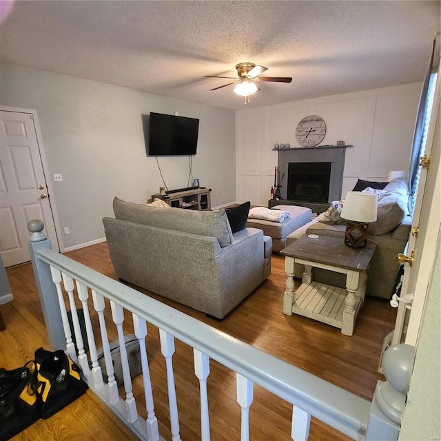 living room featuring hardwood / wood-style flooring, ceiling fan, and a textured ceiling