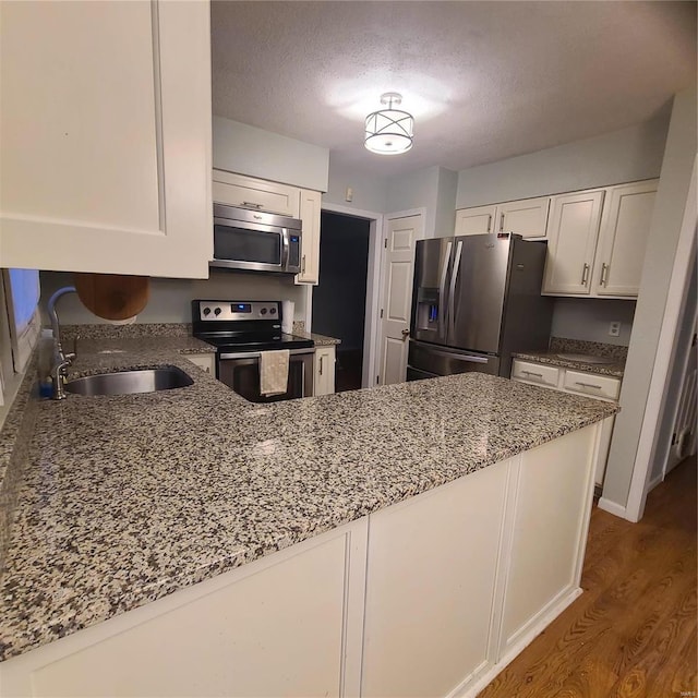 kitchen with kitchen peninsula, white cabinetry, sink, and appliances with stainless steel finishes