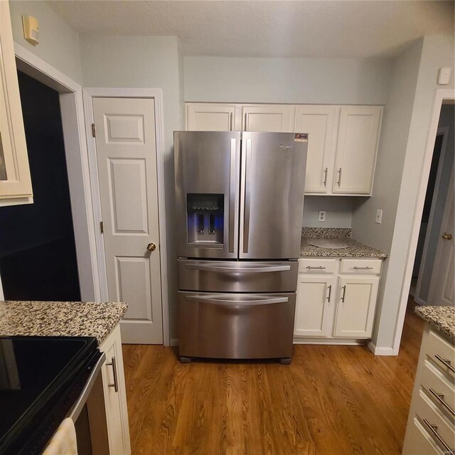 kitchen with white cabinets, stainless steel refrigerator with ice dispenser, light hardwood / wood-style floors, and light stone countertops