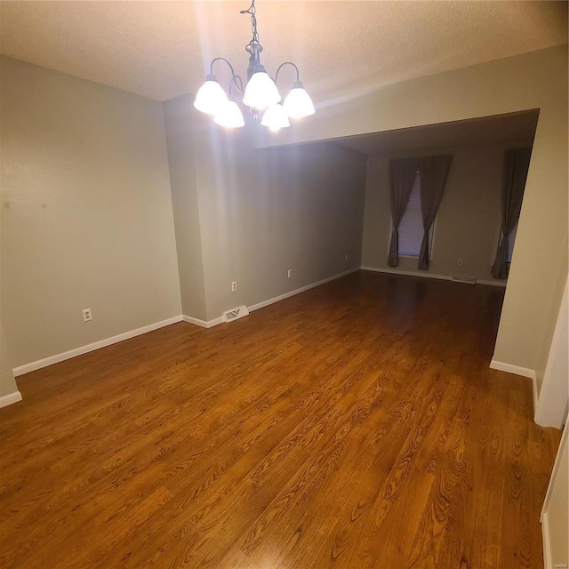 empty room with dark wood-type flooring, a textured ceiling, and an inviting chandelier