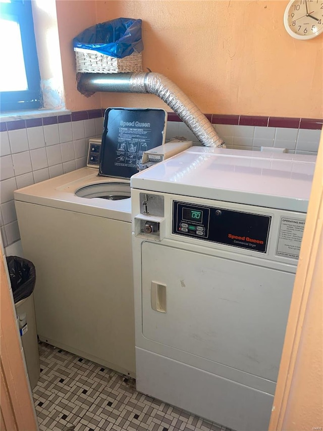 laundry room featuring light tile patterned floors, washer and dryer, and tile walls