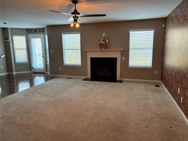 unfurnished living room with brick wall, carpet flooring, and ceiling fan