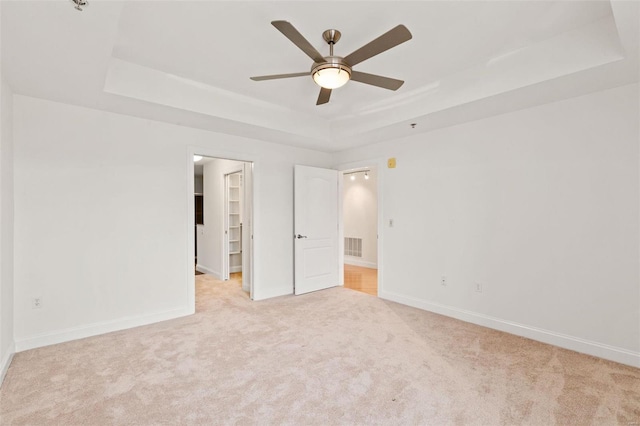 unfurnished bedroom with a tray ceiling, a walk in closet, ceiling fan, and light carpet