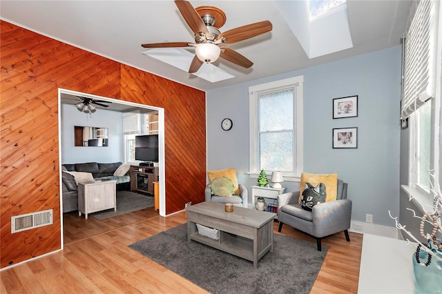 living room with a skylight, wood walls, ceiling fan, and light wood-type flooring