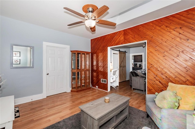 living room featuring wood walls, ceiling fan, a barn door, and hardwood / wood-style floors