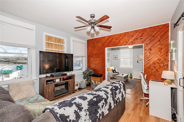 living room with wood walls, ceiling fan, and light wood-type flooring