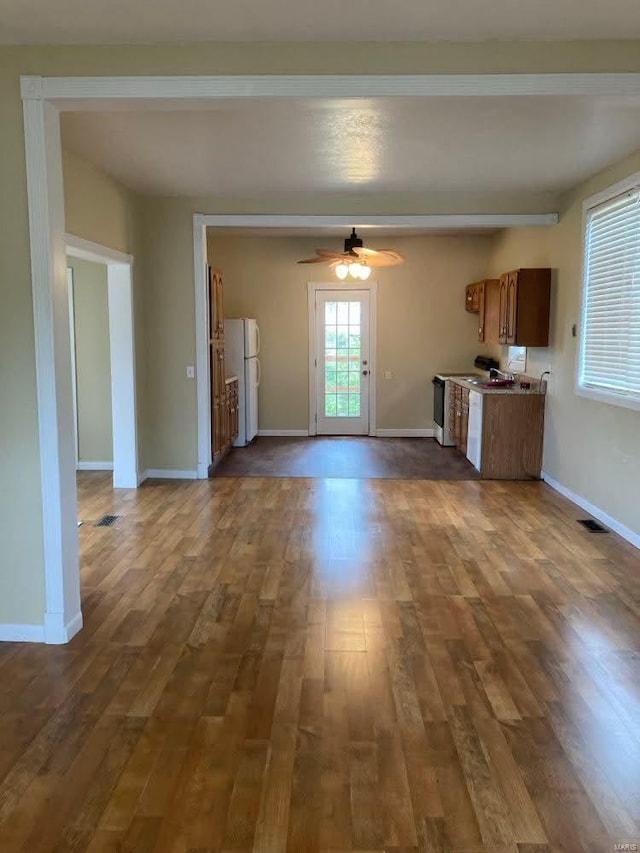 unfurnished living room featuring beamed ceiling, ceiling fan, and dark wood-type flooring