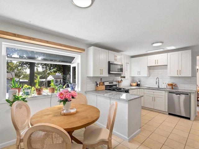 kitchen featuring white cabinetry, sink, light stone countertops, light tile patterned floors, and appliances with stainless steel finishes