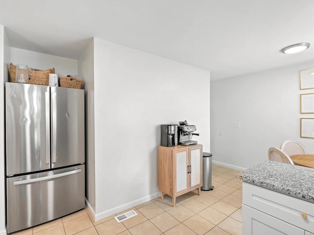 kitchen featuring white cabinets, light tile patterned floors, light stone countertops, and stainless steel refrigerator