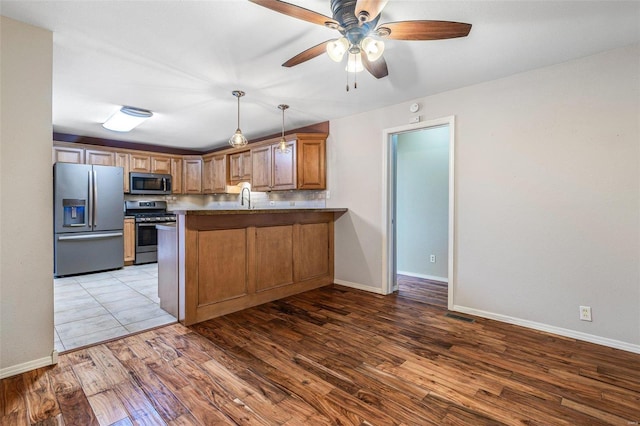 kitchen with pendant lighting, sink, appliances with stainless steel finishes, wood-type flooring, and kitchen peninsula