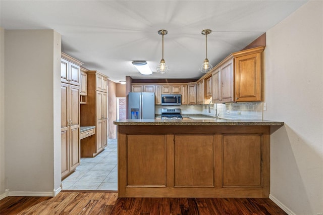 kitchen with light hardwood / wood-style flooring, appliances with stainless steel finishes, backsplash, decorative light fixtures, and kitchen peninsula