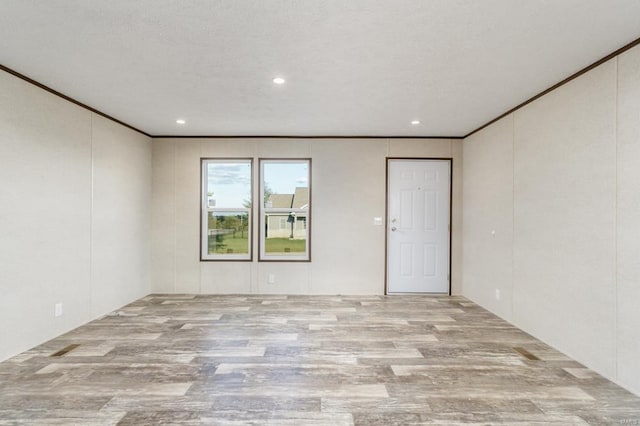 empty room with crown molding, a textured ceiling, and light wood-type flooring