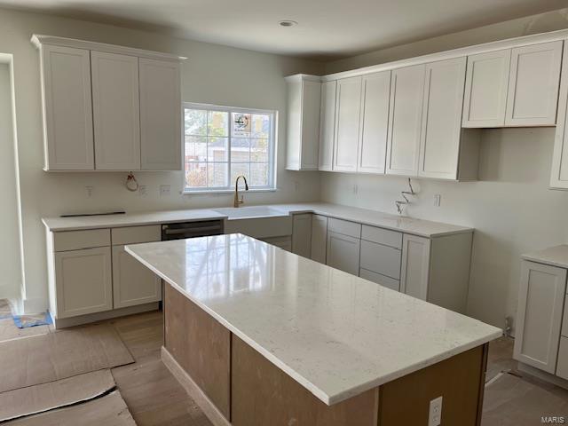 kitchen featuring a sink, light stone counters, white cabinets, and a center island