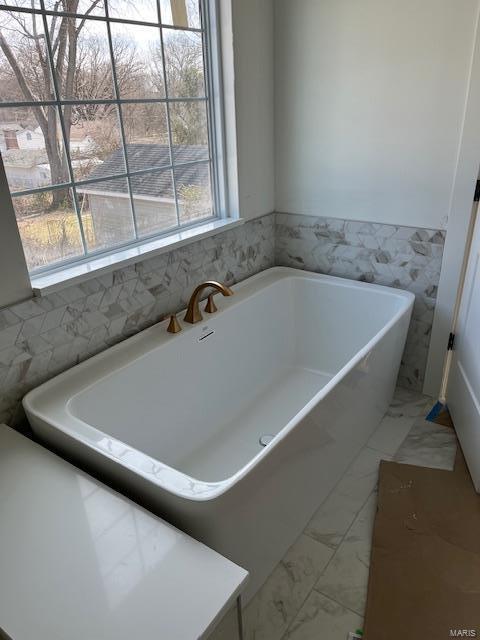 bathroom featuring a soaking tub and marble finish floor