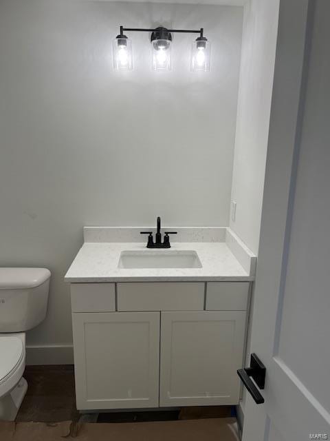 half bathroom featuring toilet, vanity, and baseboards