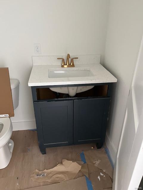 half bath featuring vanity, toilet, wood finished floors, and baseboards