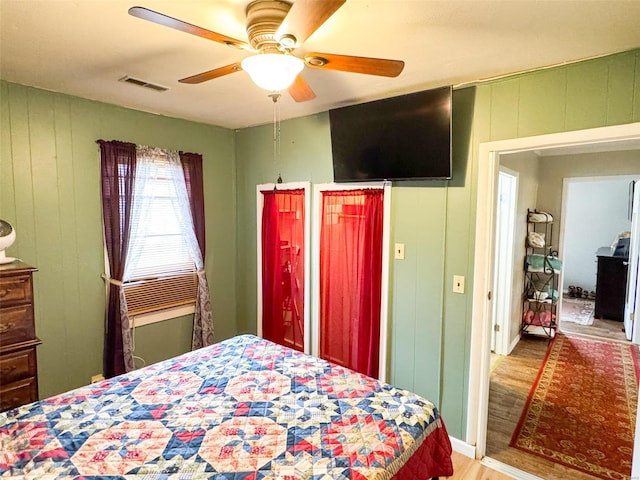 bedroom featuring hardwood / wood-style flooring, ceiling fan, and wooden walls