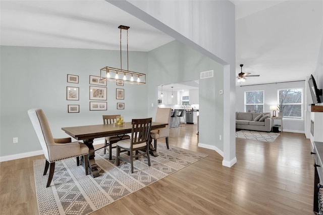 dining space with ceiling fan, high vaulted ceiling, and light hardwood / wood-style flooring