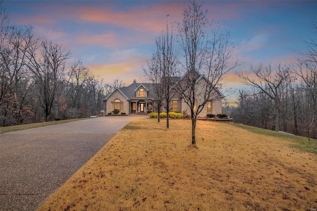 view of front of home featuring stone siding, a chimney, a front lawn, and aphalt driveway