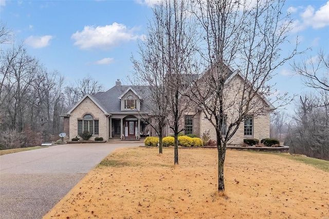 view of front of property featuring aphalt driveway, brick siding, and a chimney