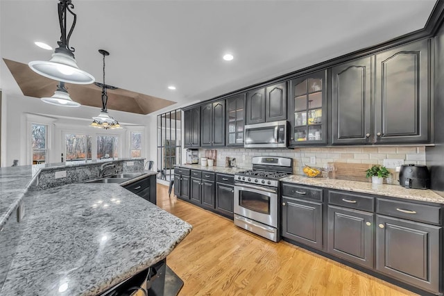 kitchen featuring light wood-style flooring, stainless steel appliances, a sink, hanging light fixtures, and decorative backsplash