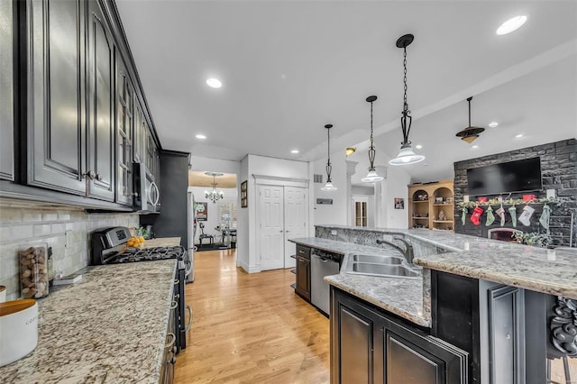 kitchen featuring appliances with stainless steel finishes, decorative light fixtures, a sink, light wood-style floors, and backsplash