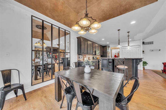 dining area featuring visible vents, baseboards, lofted ceiling, light wood-type flooring, and a chandelier