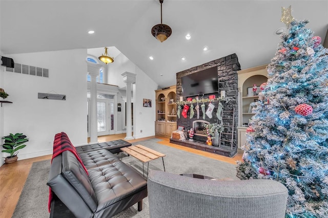 living room featuring built in shelves, decorative columns, a fireplace, visible vents, and wood finished floors