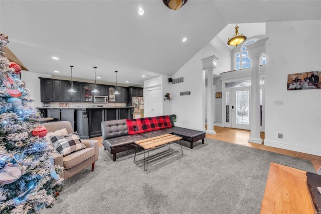 living area featuring decorative columns, baseboards, light wood-type flooring, high vaulted ceiling, and recessed lighting