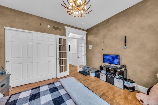 bedroom with visible vents, a chandelier, wood finished floors, and french doors