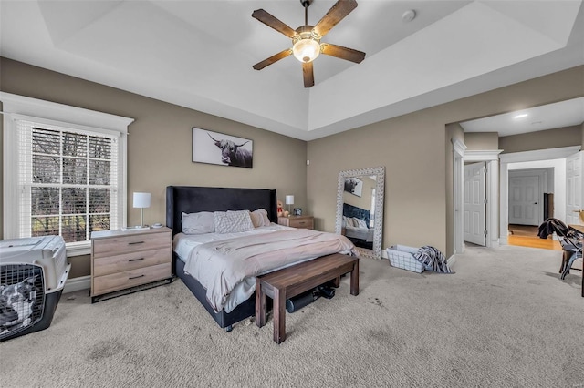 carpeted bedroom featuring a raised ceiling, a ceiling fan, and baseboards